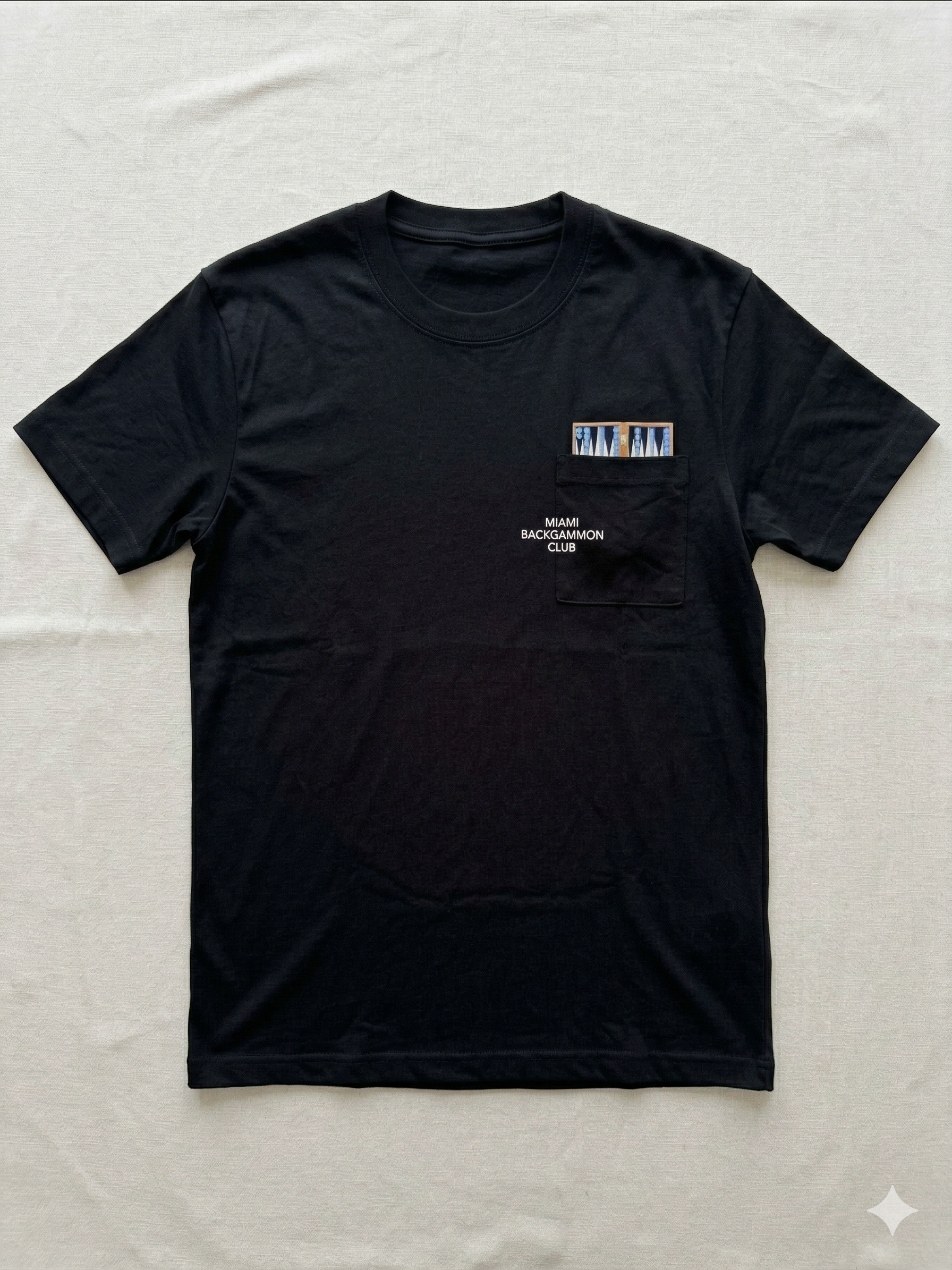 Flat lay of the Stealth Black Pocket Tee with backgammon board graphic and Miami Backgammon Club logo printed on the chest pocket