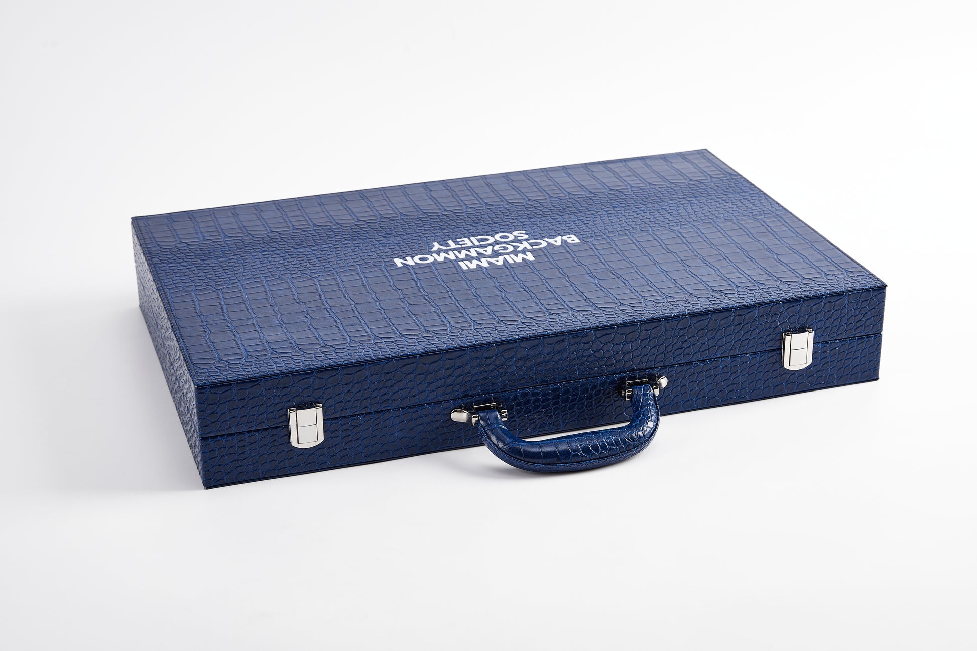 Closed Midnight Navy crocodile-embossed backgammon case with Miami Backgammon Society branding, carry handle, and silver clasps