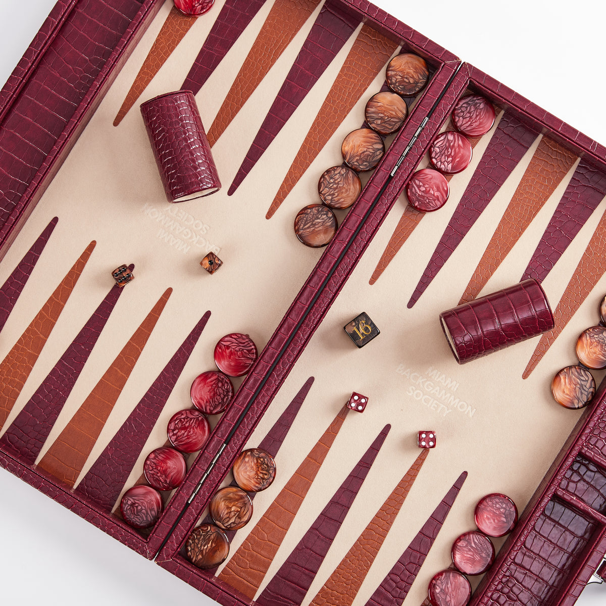 Open Bordeaux burgundy crocodile-embossed backgammon board set up with checkers, dice, and dice cups
