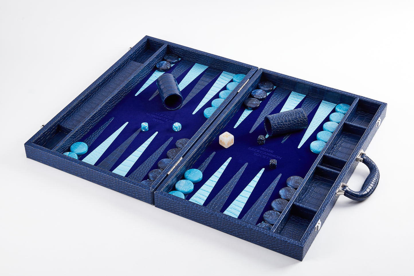 Elevated angled view of Midnight Navy backgammon board mid-play with dice cups, doubling cube, and checkers scattered on the field