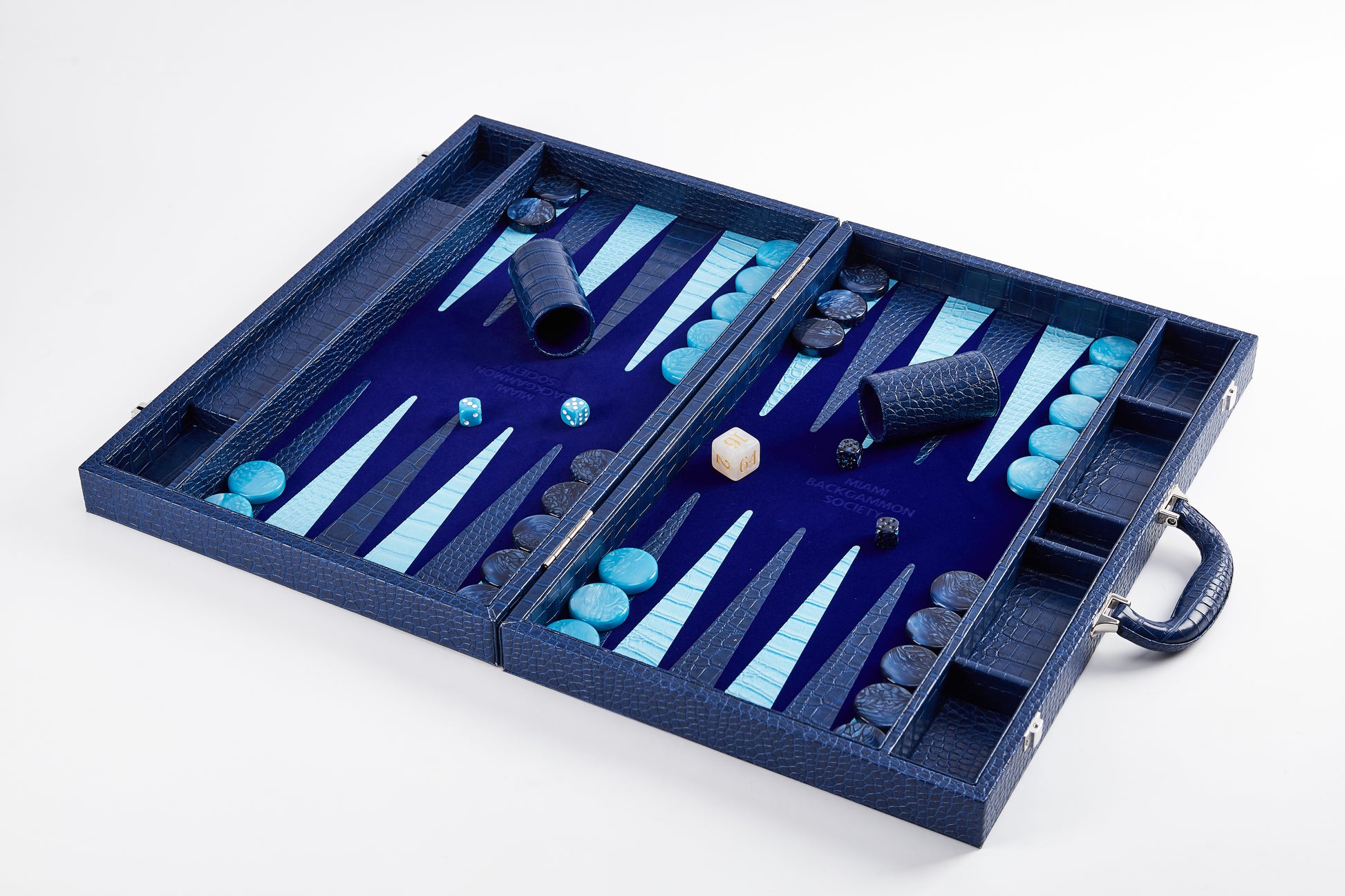Elevated angled view of Midnight Navy backgammon board mid-play with dice cups, doubling cube, and checkers scattered on the field