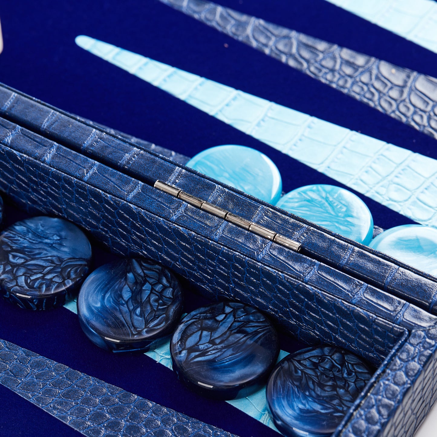 Macro close-up of the board's hinge with cyan and navy checkers on either side, showing crocodile-embossed texture detail