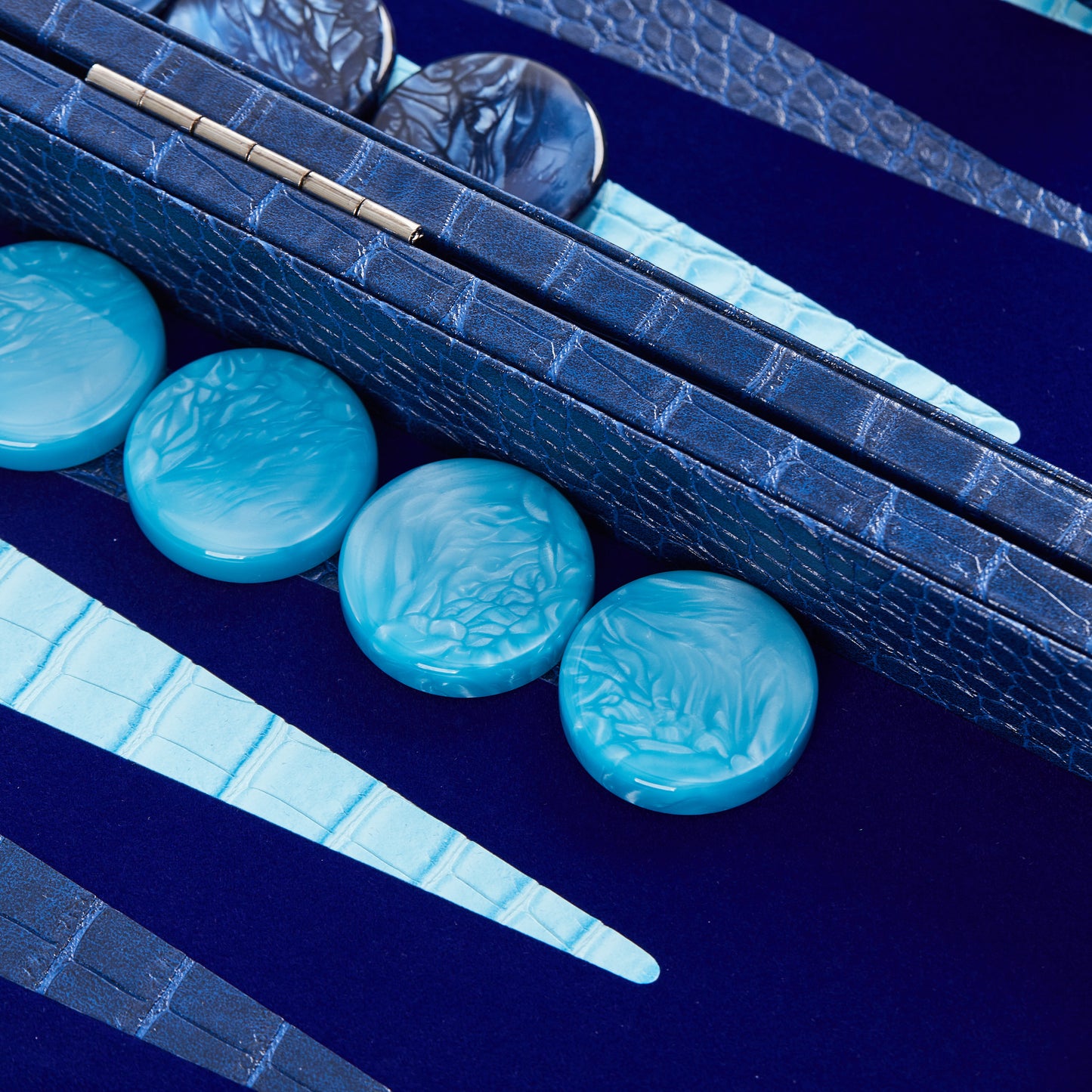 Macro close-up of cyan checkers resting on the Midnight Navy backgammon board's cyan-tipped triangular points