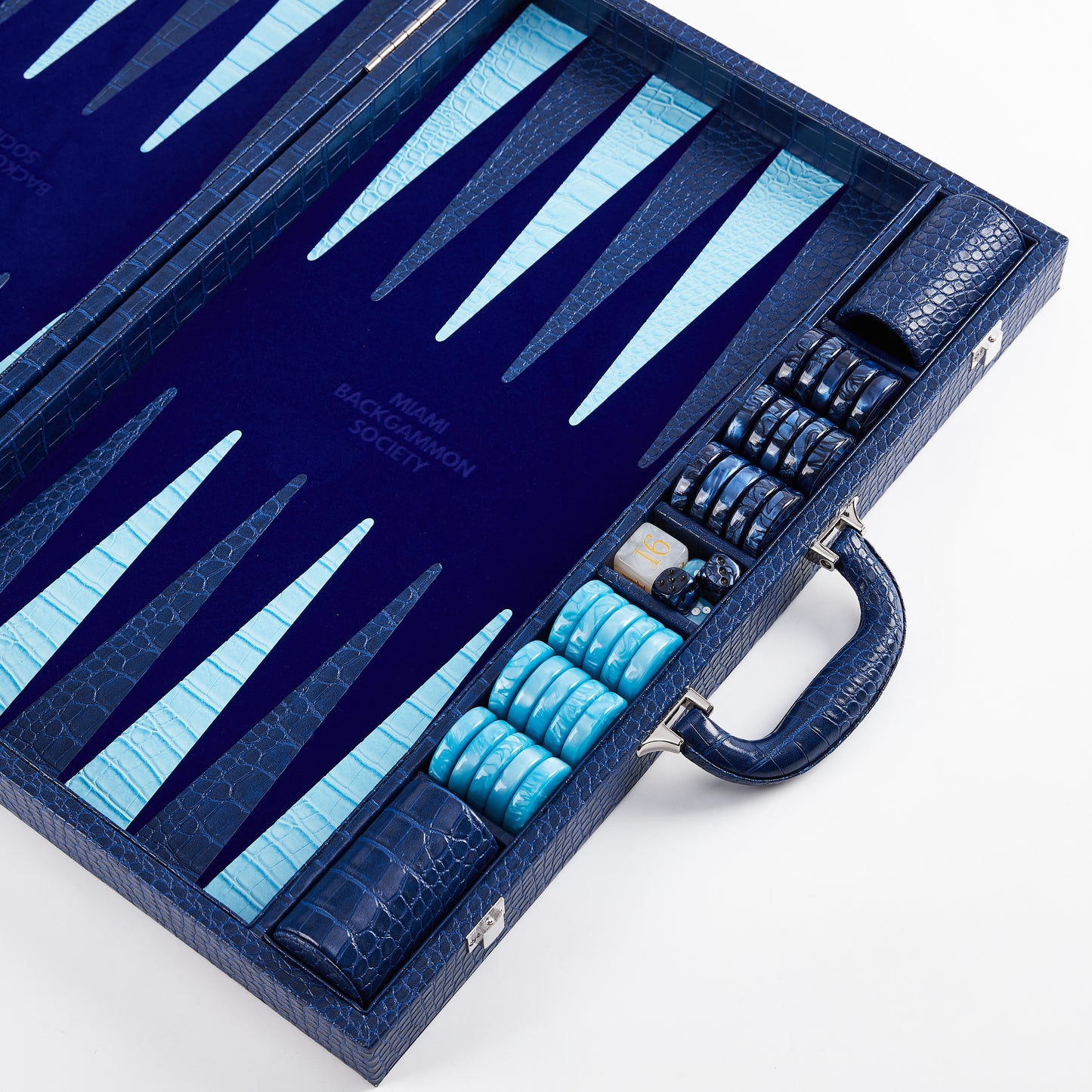 Angled view of open Midnight Navy backgammon case showing stacked navy and cyan checkers, doubling cube, and dice cup in the storage tray with carry handle
