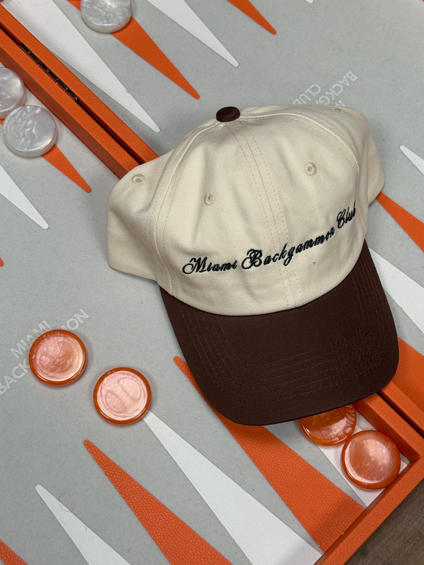 Orange Miami Backgammon Club board with dice and chips, featuring the club’s embroidered hat.
