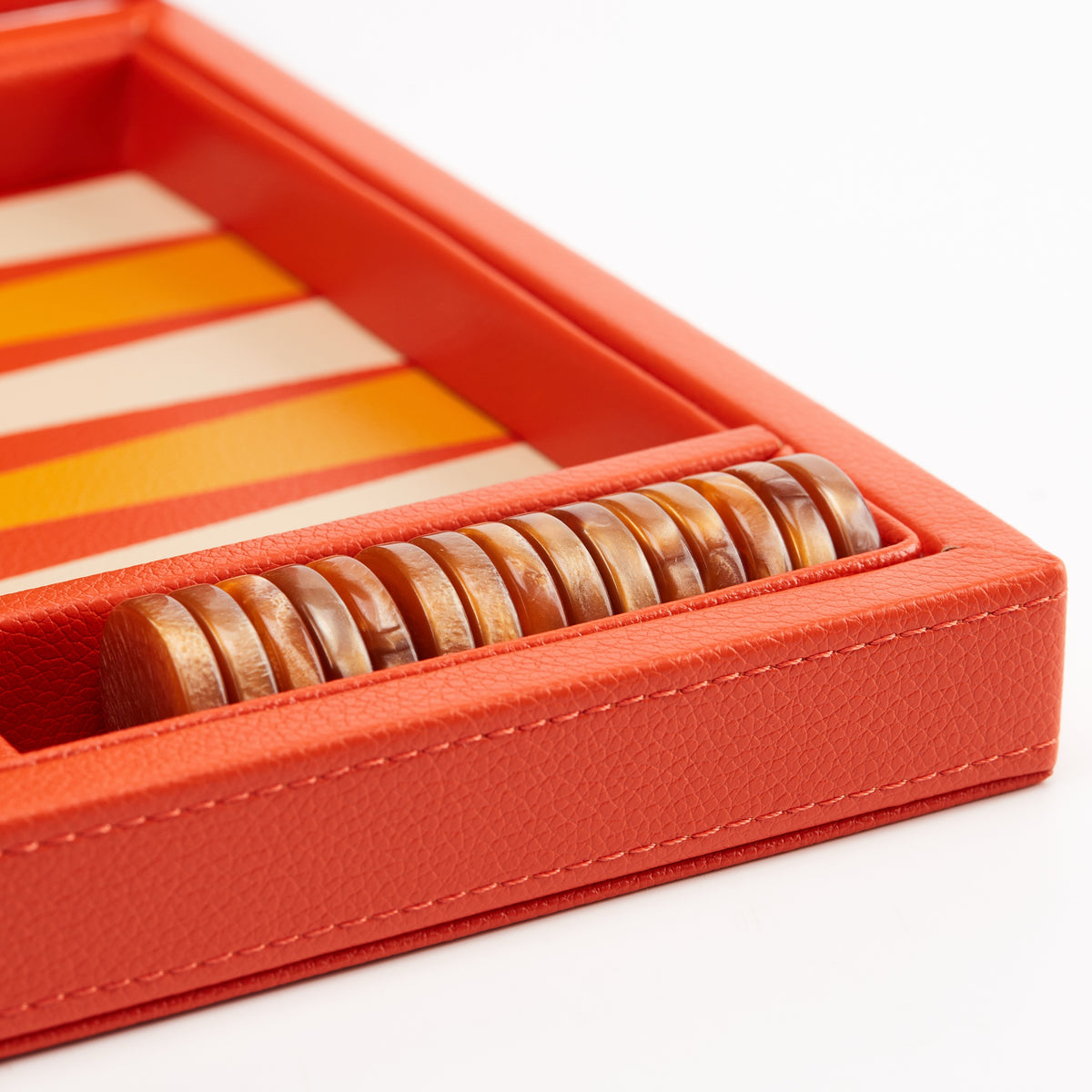 Bronze checkers stacked in the side tray of the orange board